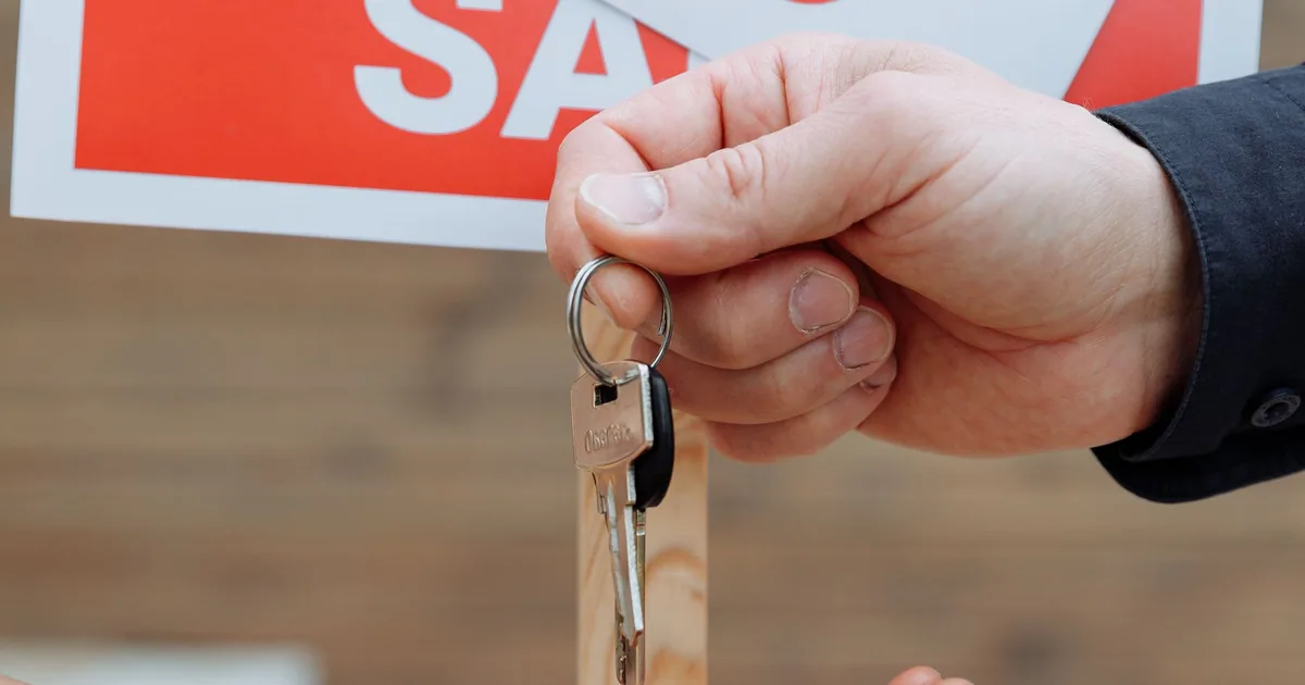 A hand holding house keys beside a sold sign after a successful transaction