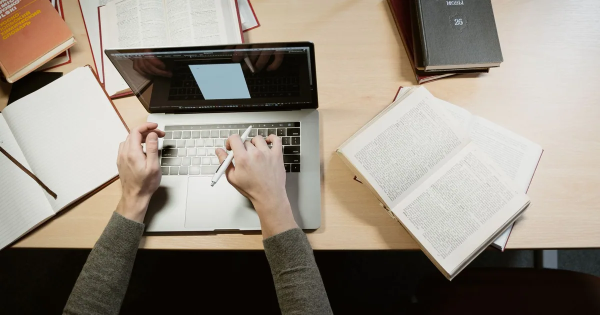 A student researching course information on a laptop beside open reference books