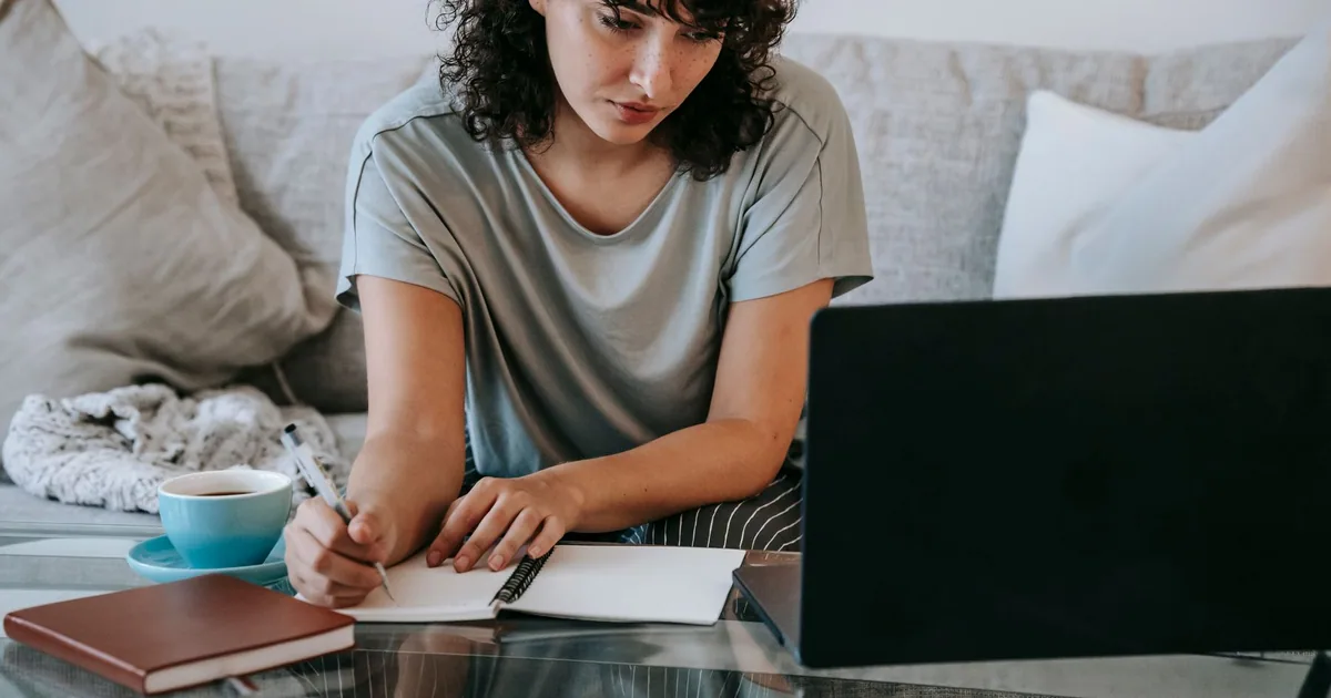 A student taking notes while completing an online course on a laptop