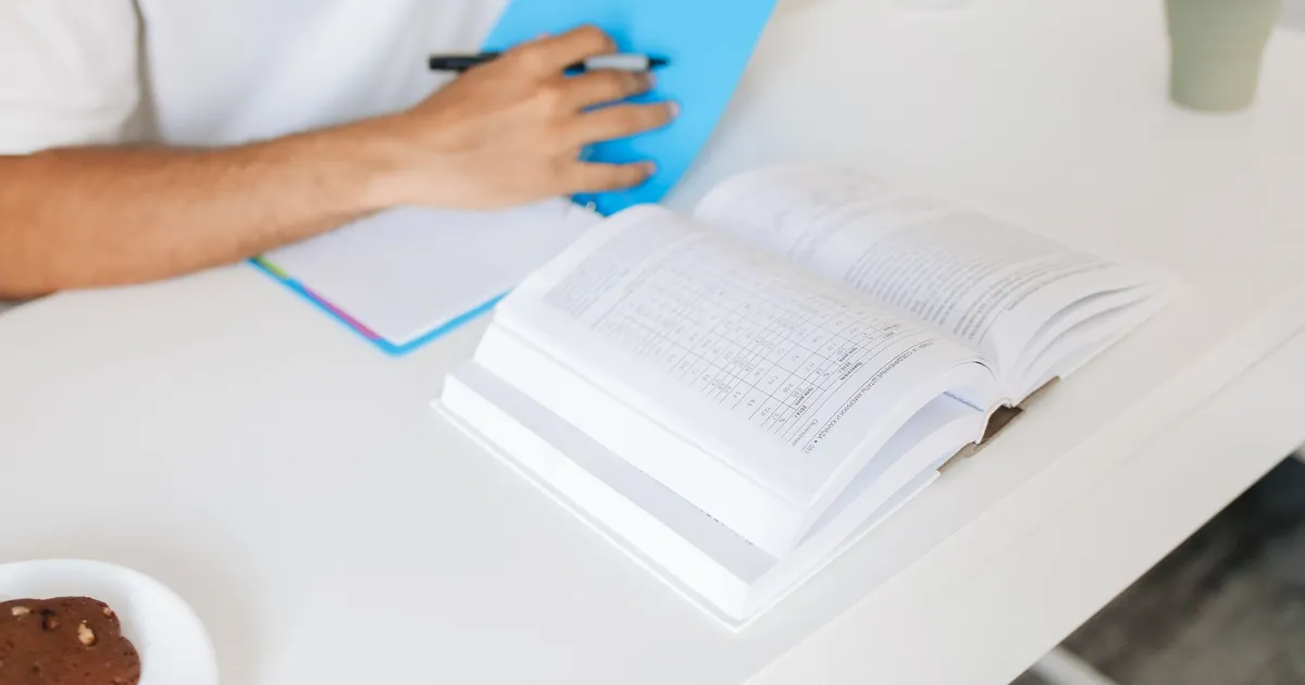 A student reviewing an open textbook and taking notes